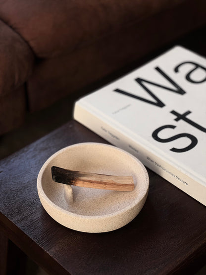 Small beige dish with a wooden spatula on a dark surface next to a book.